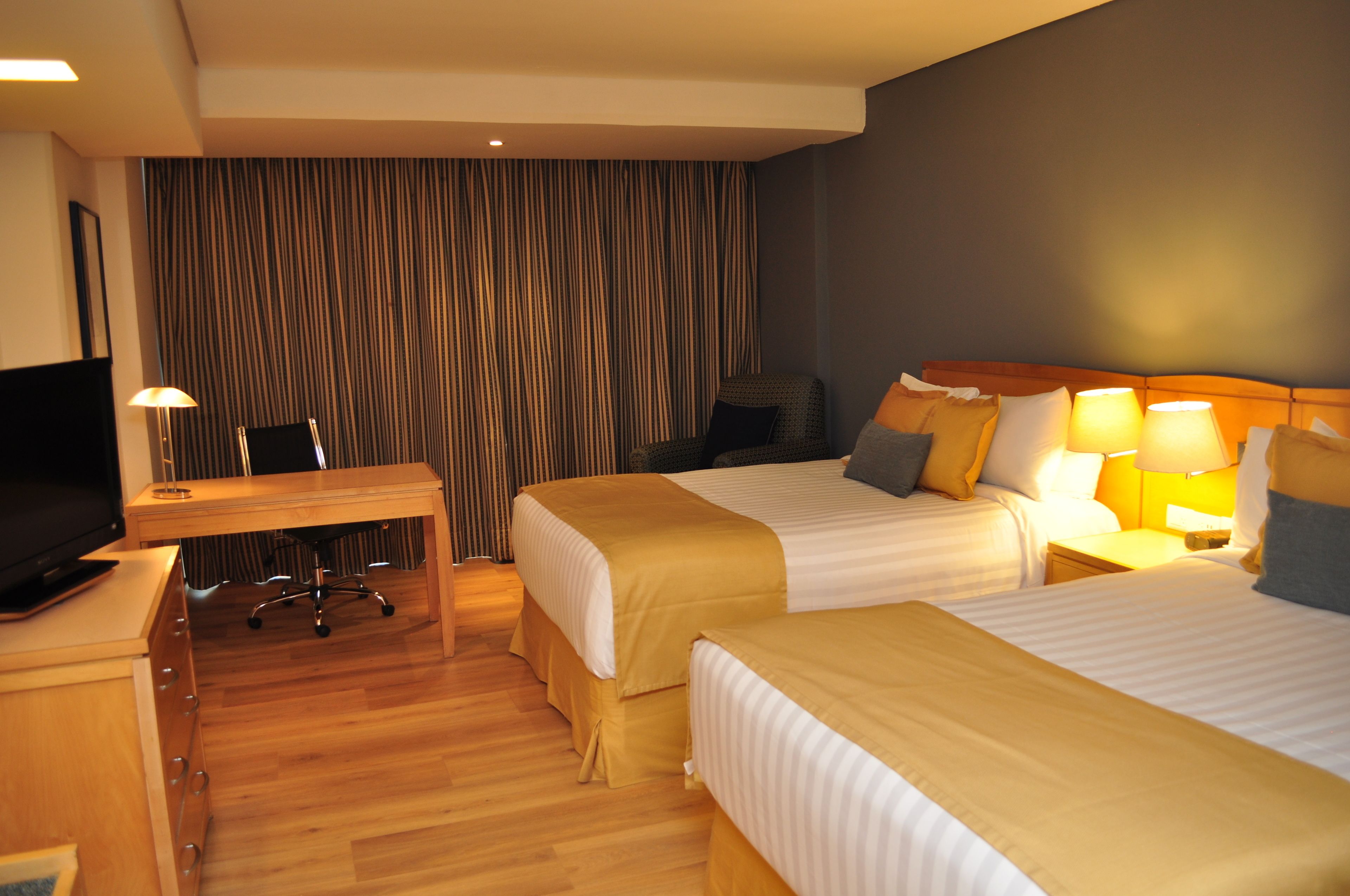 A hotel room with two beds, a desk, a TV, and a curtain backdrop.