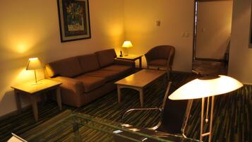 A hotel room with a sofa, a chair, a small table, and a glass partition.
