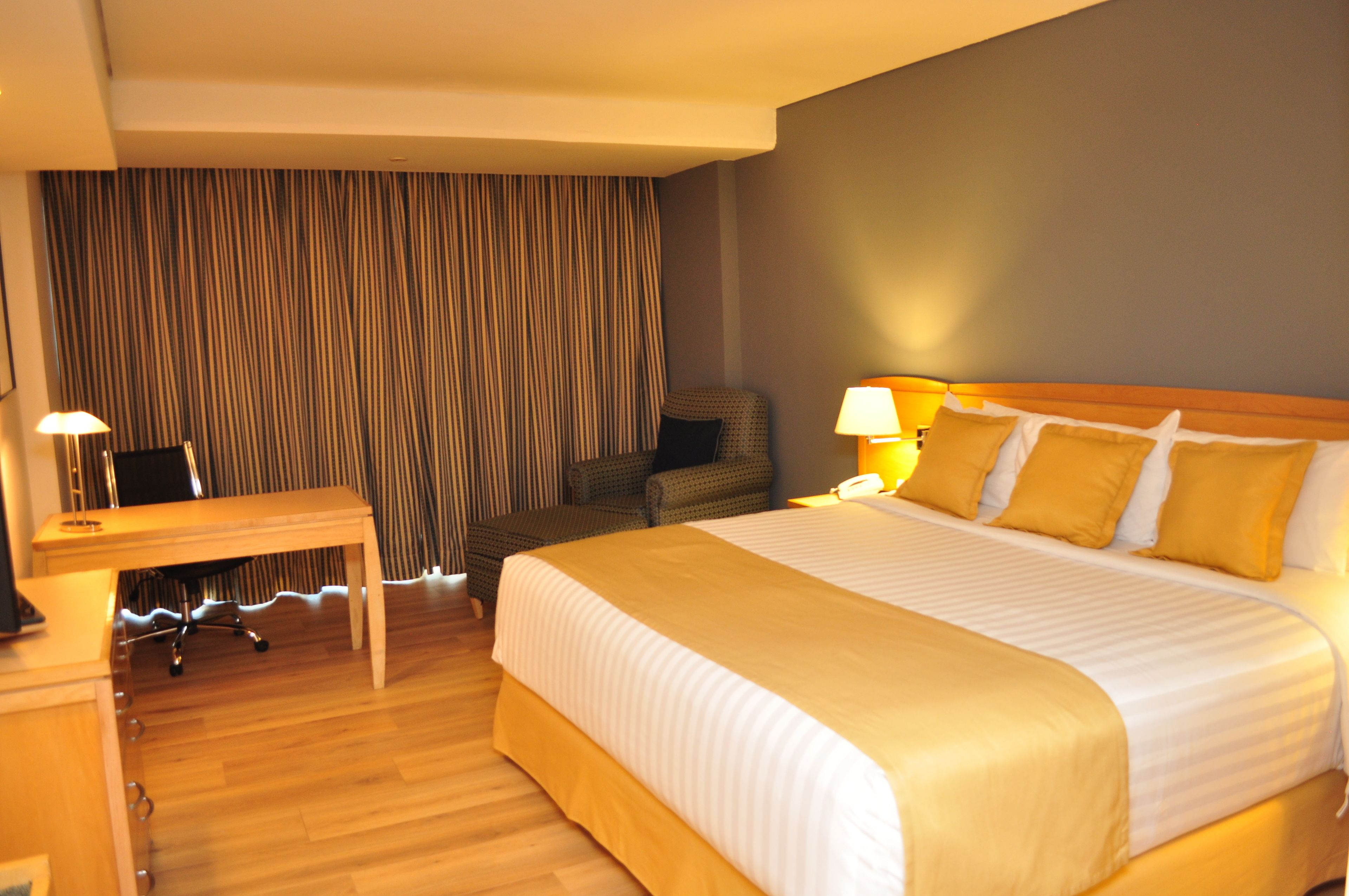 Une chambre d’hôtel avec un grand lit, un bureau, une chaise et un rideau.