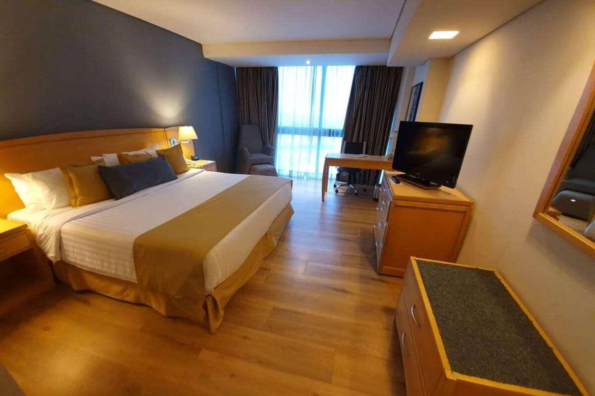 A hotel room with a large bed, a desk with a TV, and a view of the outdoors.