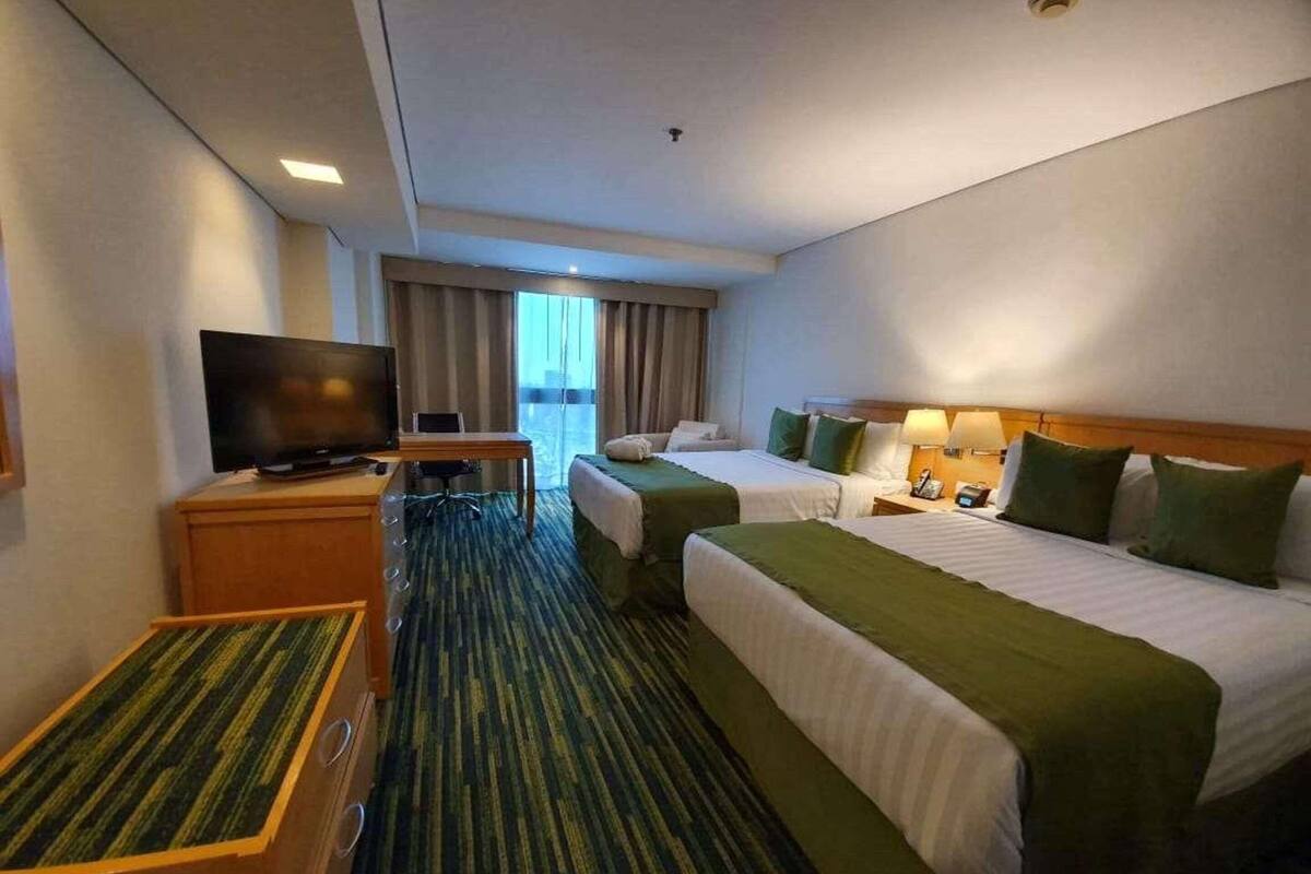 A hotel room with two beds, a desk with a television, a chair, and a small table.