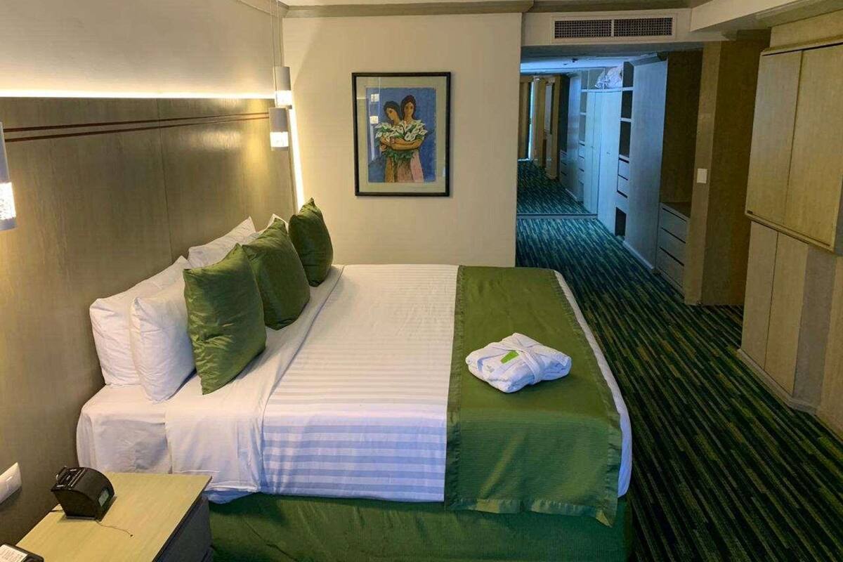 A hotel room with a bed, pillows, a blanket, a painting on the wall, and a desk with a telephone.