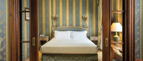 Una habitación de hotel con una cama grande, una mesita de noche con lámpara y una pared con rayas verticales.