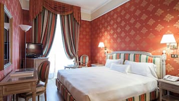 Habitación de hotel con cama, escritorio, silla, televisor y lámparas.