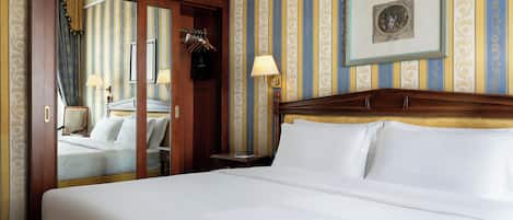 A hotel room with a large bed, a wooden headboard, a mirror, a framed picture on the wall, and a door with a mirror and clothes hanging.