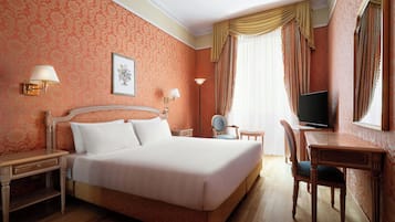 Habitación de hotel con una cama grande, dos mesitas de noche, un escritorio con silla, televisión y ventana con cortinas.