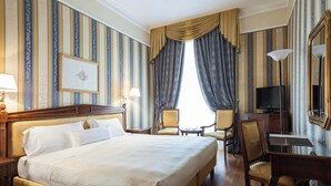 A hotel room with a large bed, two chairs, a desk, a television, and a mirror. - Sina De la Ville (Milan)