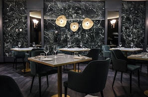Un restaurant aux murs de marbre, aux tables rondes et aux chaises modernes.