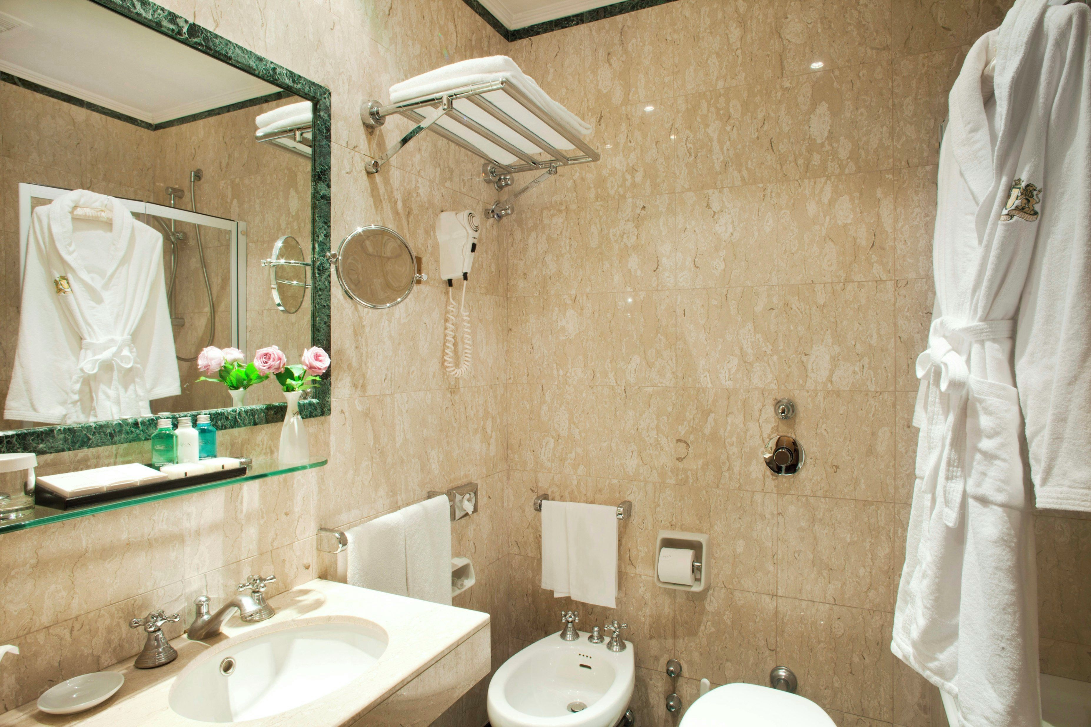 Une salle de bain équipée d’un lavabo, d’un bidet, d’un miroir, d’un porte-serviettes et d’une robe accrochée au mur.