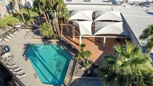 An aerial view of a hotel with a swimming pool, outdoor seating, and palm trees.