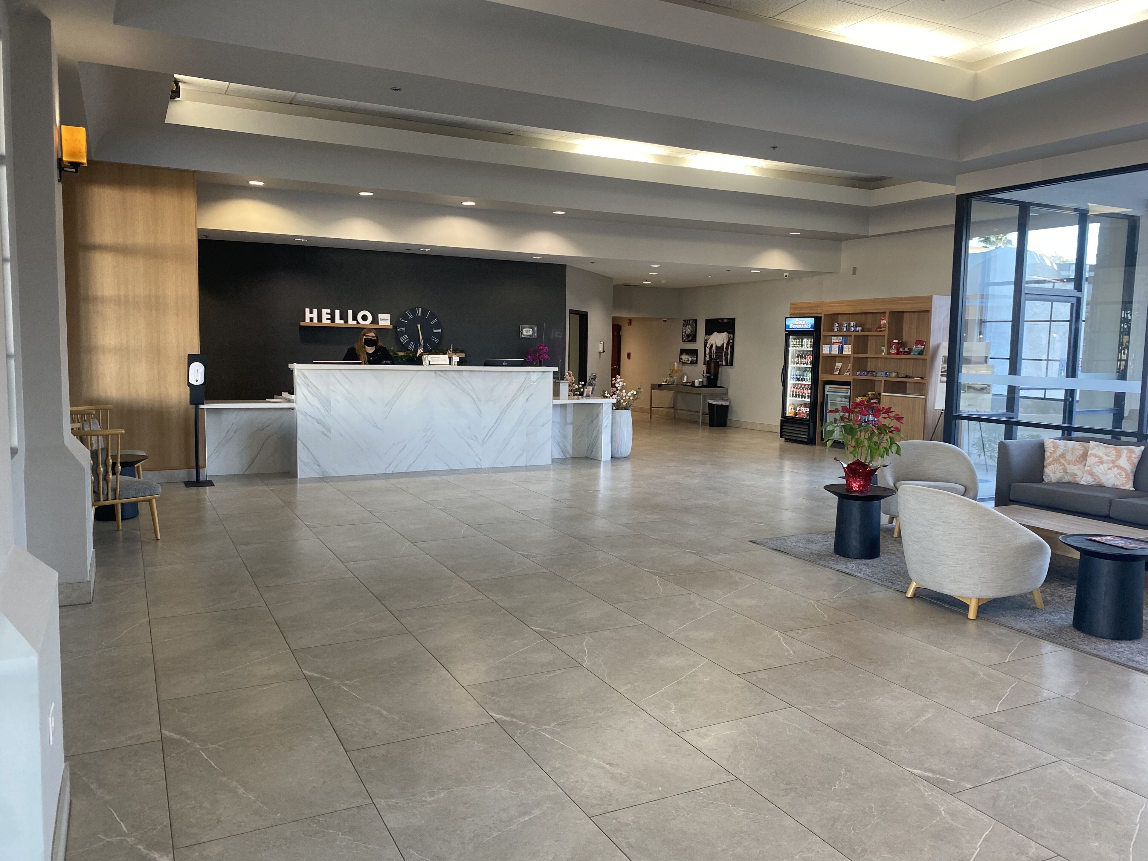 Un hall d’hôtel moderne avec un comptoir d’accueil en marbre, un espace salon et de grandes fenêtres.
