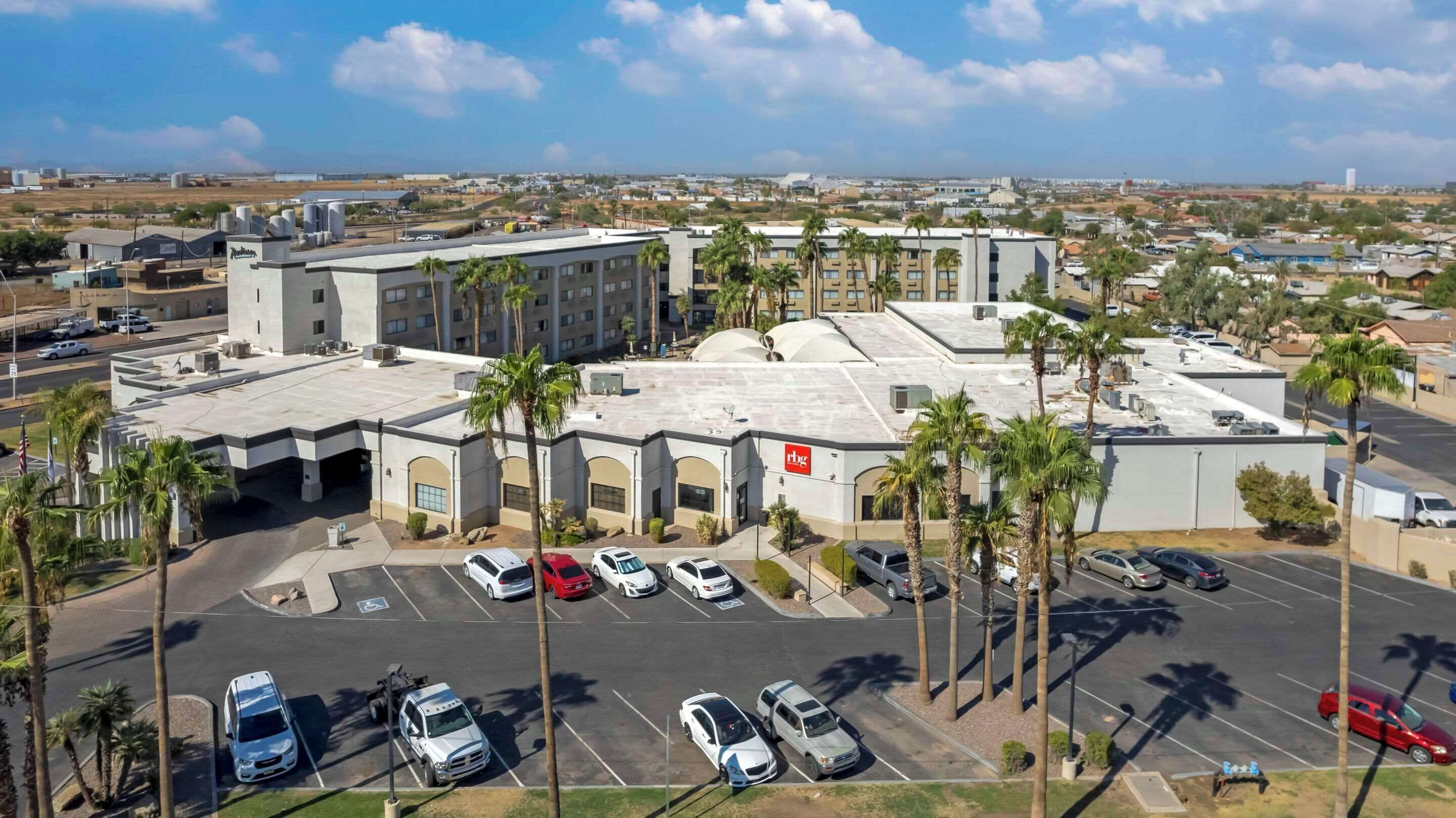 A multi-story hotel with a parking lot, palm trees, and a clear sky.