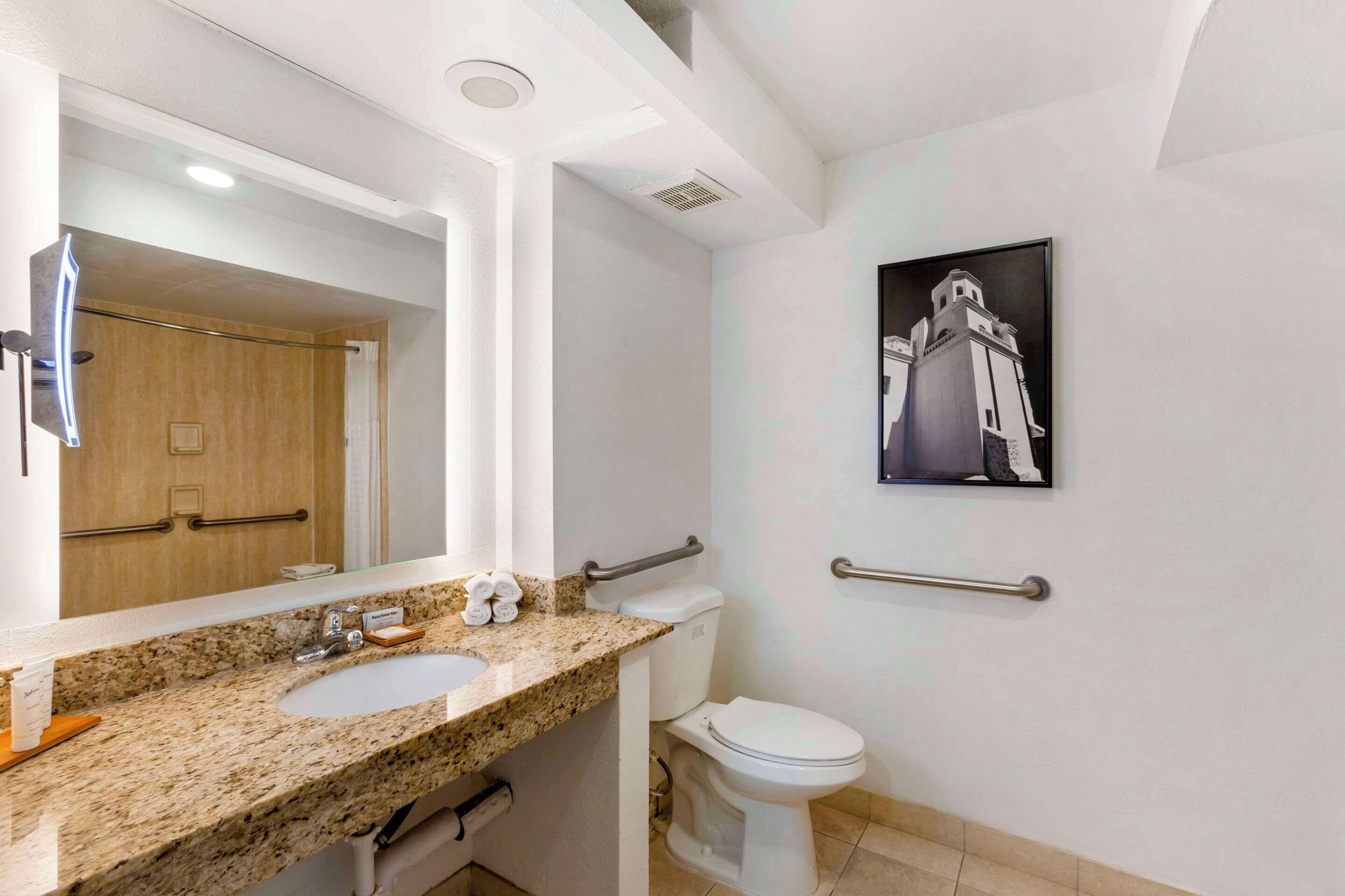 A bathroom with a granite countertop sink, a white toilet, and a handrail.