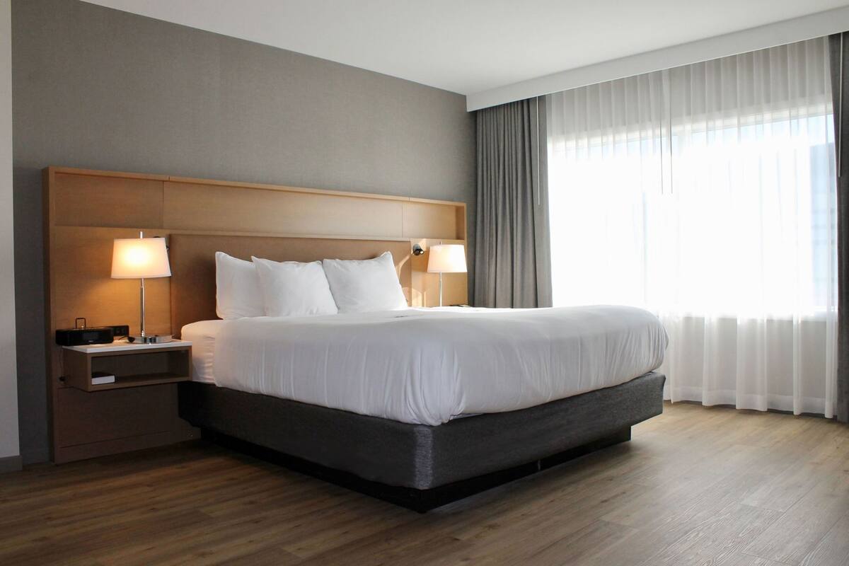 Una habitación de hotel moderna con una cama grande, dos lámparas de noche, una mesita de noche y una ventana con cortinas.