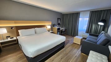 A hotel room with a large bed, a desk with a chair, a sofa, and a small ottoman.