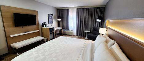 A hotel room with a large bed, a desk, a chair, a TV, a small table, and a lamp.