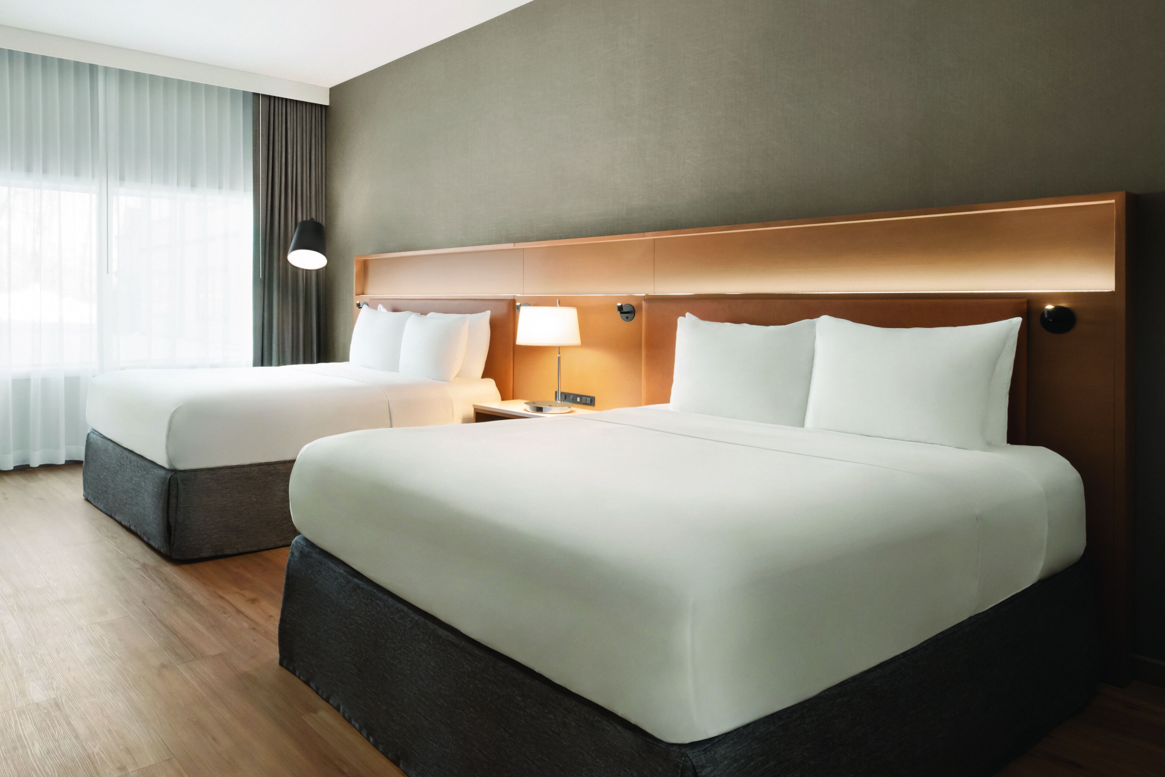 Habitación de hotel con dos camas, una mesita de noche, una lámpara y una ventana con cortinas.