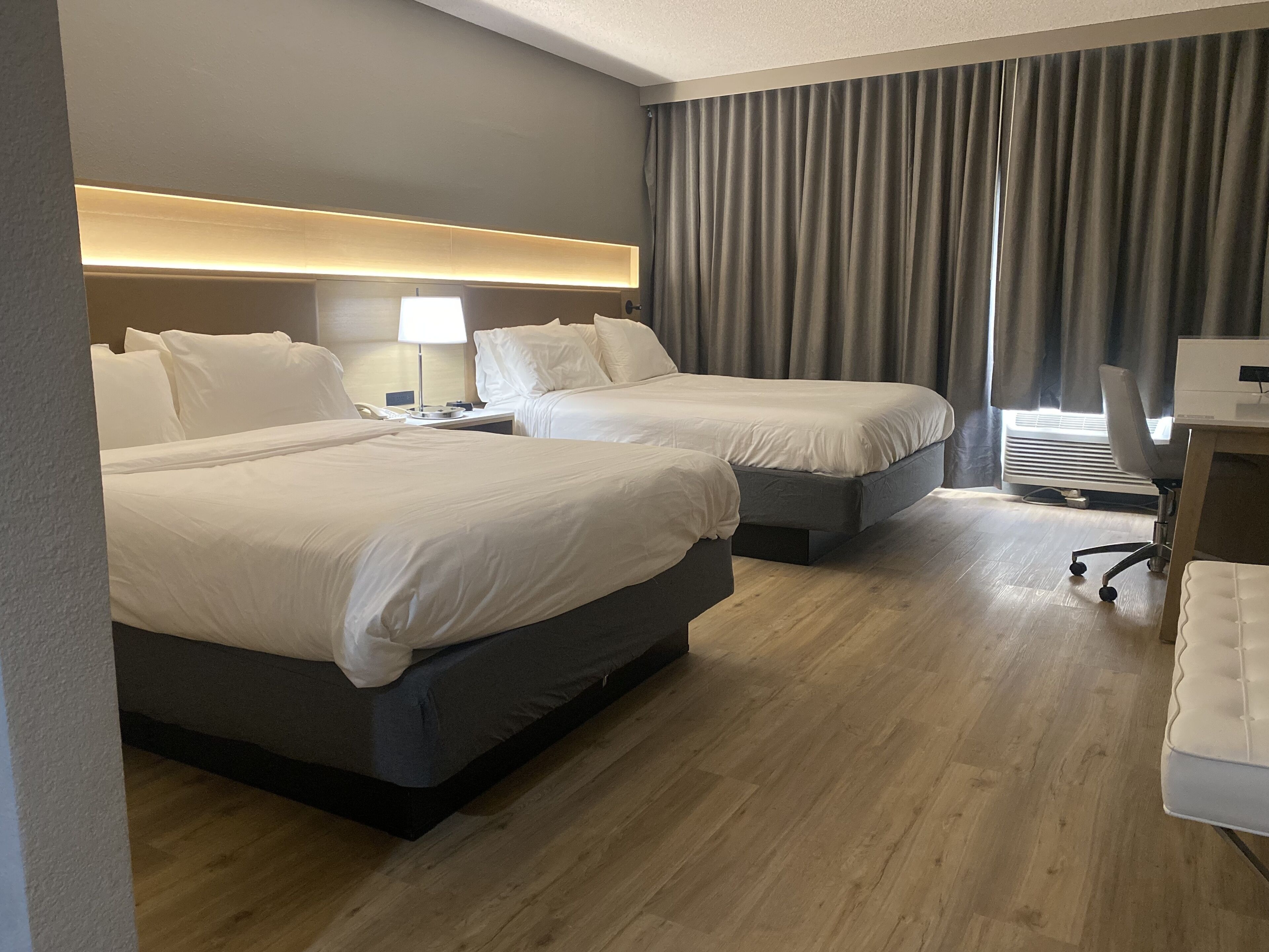 Ein Hotelzimmer mit zwei Betten, einem Schreibtisch, einem Stuhl, einer Lampe und einem Fenster mit Vorhängen.