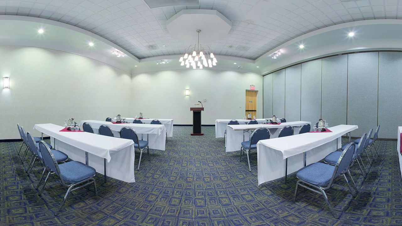 A conference room with tables and chairs, a podium, and a patterned carpet.
