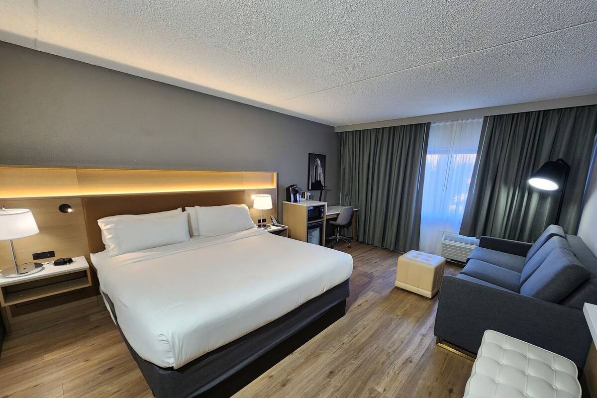 Habitación de hotel con cama, escritorio, silla, sofá y un pequeño otoman.