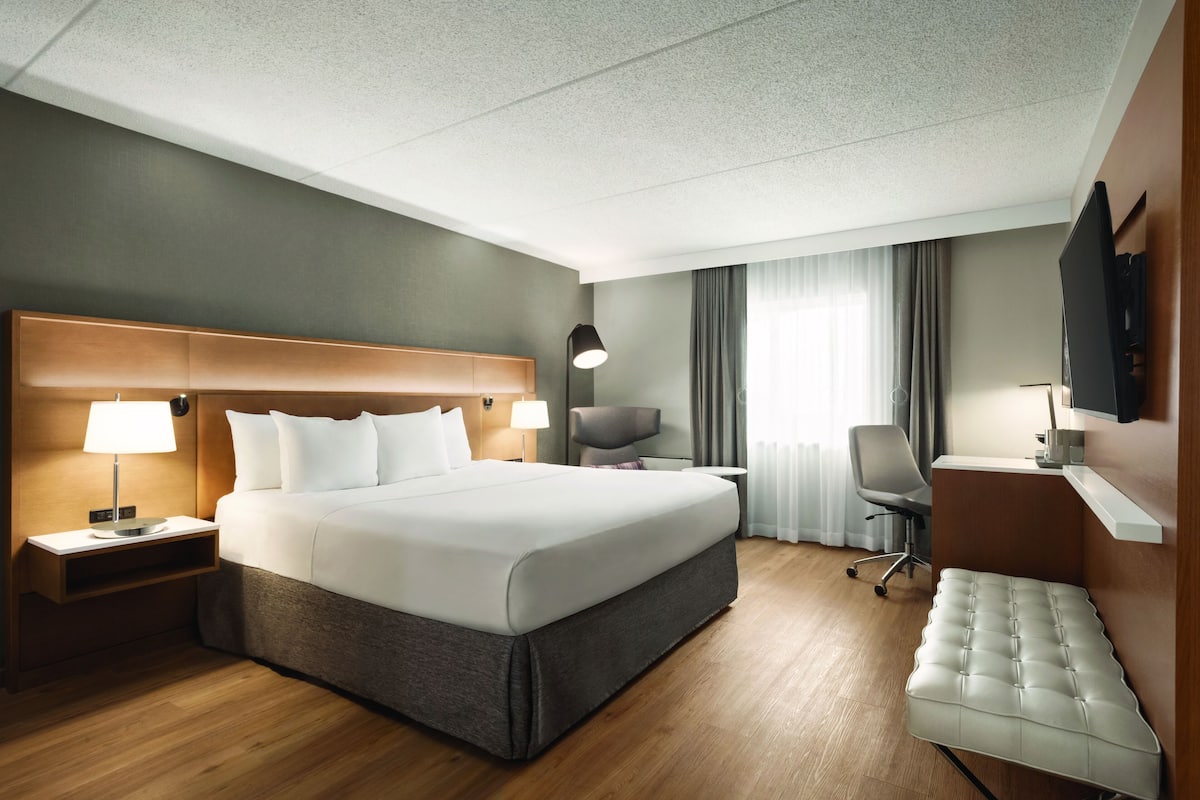 Habitación de hotel con una cama grande, mesitas de noche, un escritorio, una silla, un televisor y una ventana con cortinas.