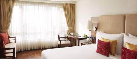 Una habitación de hotel con una cama grande, un escritorio, una silla y una ventana con cortinas traslúcidas.