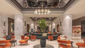 A modern lobby with marble walls, a central plant, orange and green seating, and a chandelier. - President, Mumbai - IHCL SeleQtions (Mumbai)