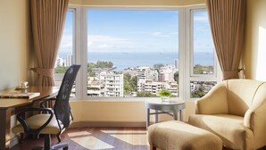 A room with a large window offering a city view, a desk with a chair, a small round table, and a sofa. - President, Mumbai - IHCL SeleQtions (Mumbai)