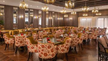 Un comedor amplio con múltiples mesas y sillas, grandes candelabros y paneles de madera.
