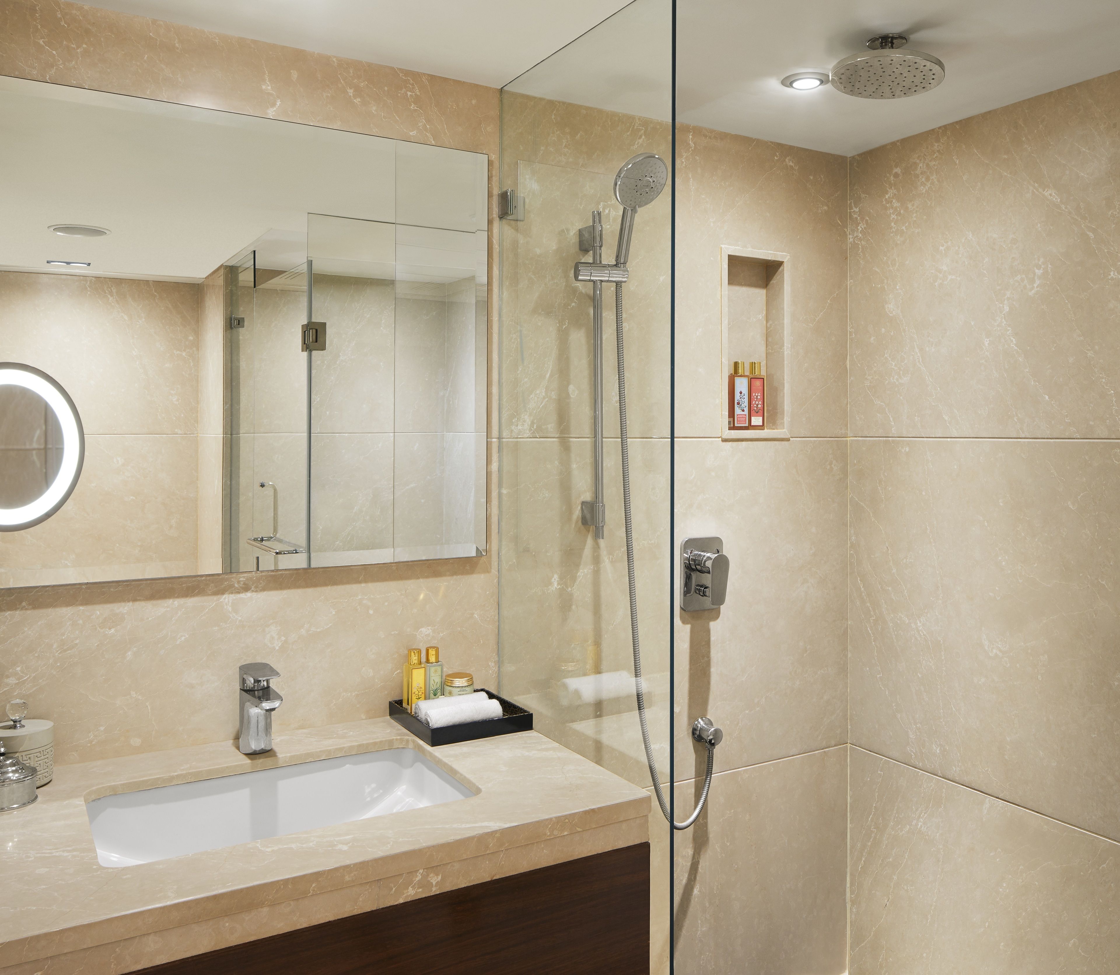 Un baño moderno con ducha envuelta en vidrio, lavamanos con artículos de aseo y espejo.