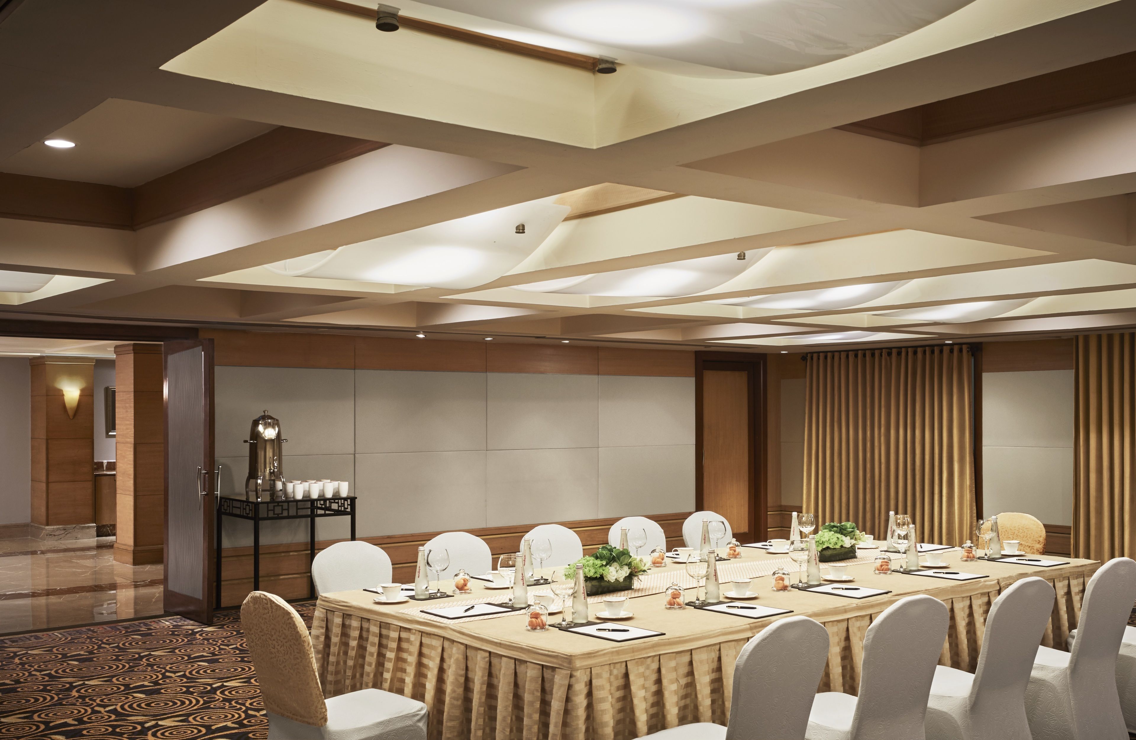 Un salón de conferencias con una larga mesa dispuesta para reuniones, equipado con sillas, mesas y diversos servicios.
