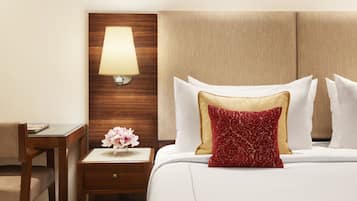 Een hotelkamer met een houten hoofdeinde, een nachtkastje met een lamp, een vaas met bloemen, en een bed met wit beddengoed en decoratieve kussens.
