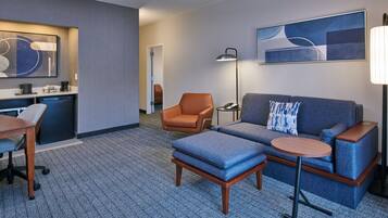 Een moderne hotelkamer met een bank, fauteuil, klein tafeltje en een bureau met lamp.