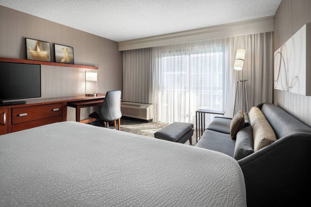 Una habitación de hotel con una cama grande, un escritorio con televisor de pantalla plana, una silla, un sofá y una lámpara.