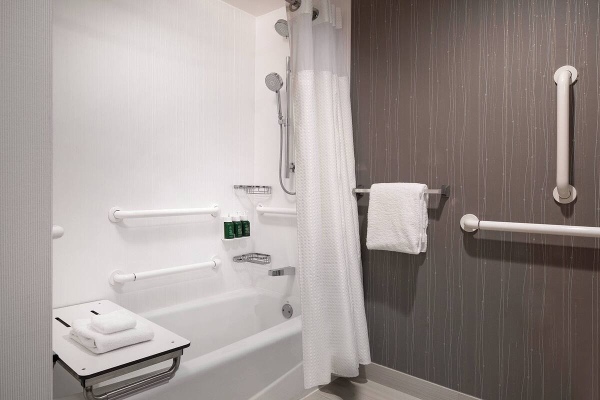 Un baño moderno con bañera, barras de apoyo, un perchero y un estante con artículos de aseo.