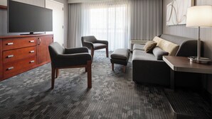 A hotel room with a flat-screen TV, a wooden cabinet, two armchairs, a sofa, a side table, and a lamp. - Courtyard San Francisco Larkspur Landing/Marin County (Larkspur)