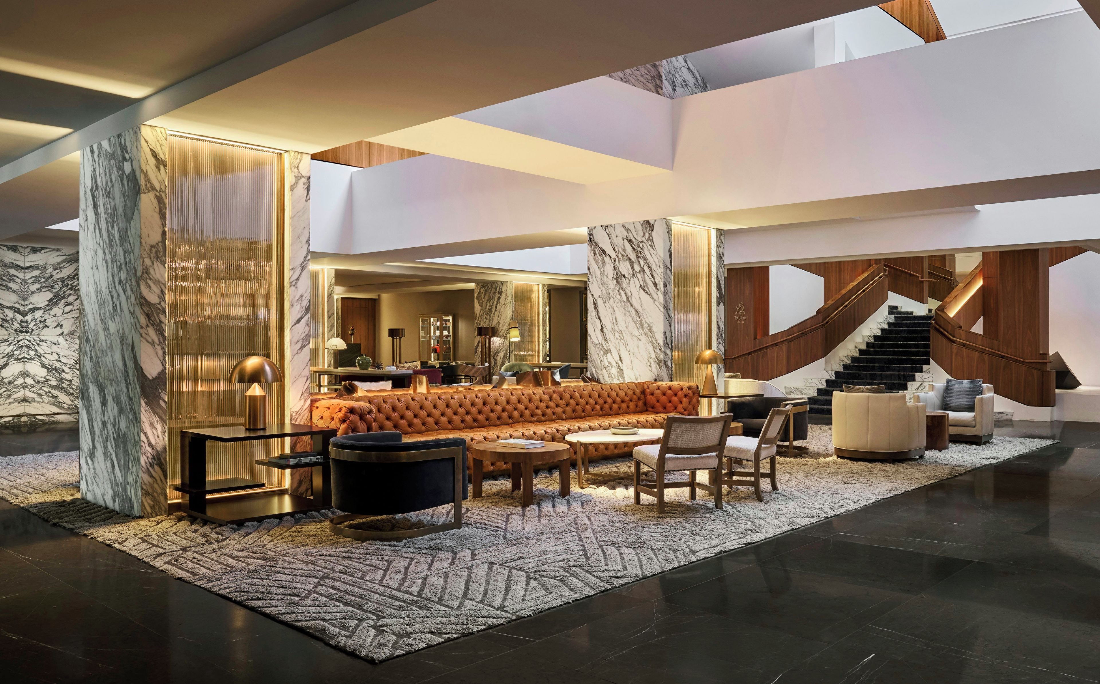 A spacious lobby with a central seating area, a staircase, and marble walls.