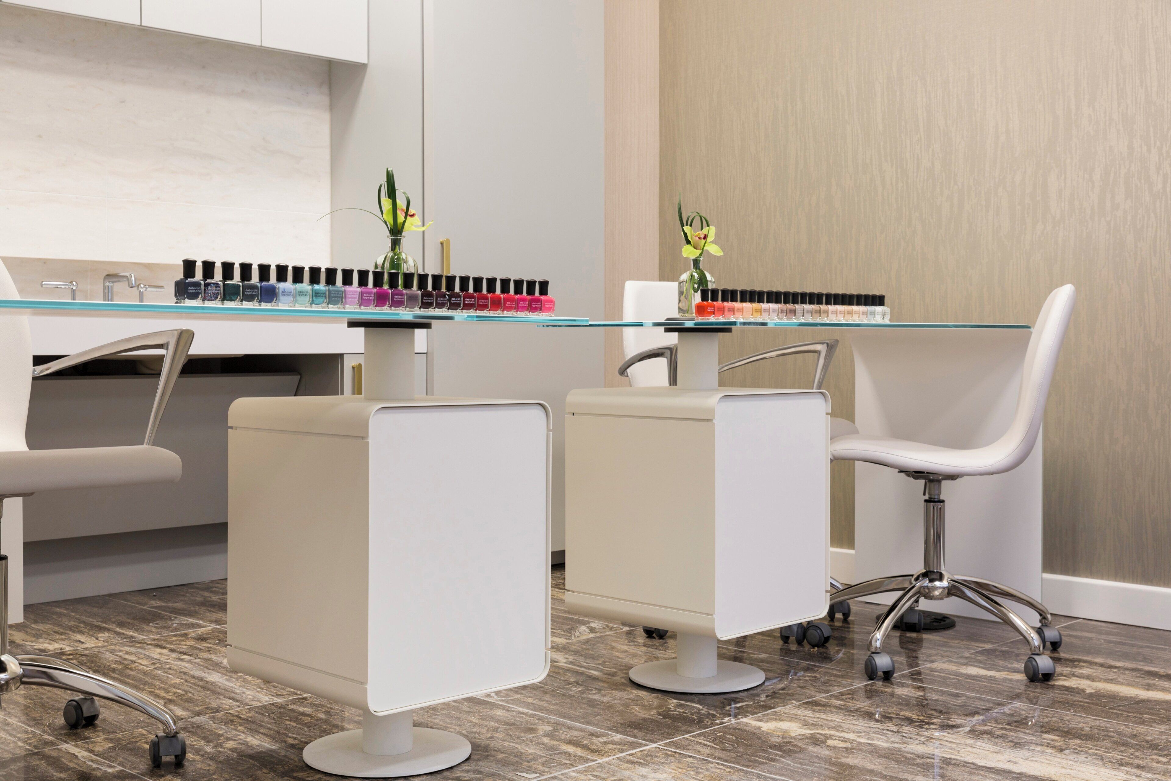 A modern salon with white chairs, a glass counter, and a selection of nail polish.