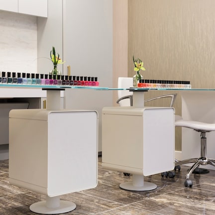 A modern salon with white chairs, a glass counter, and a selection of nail polish.