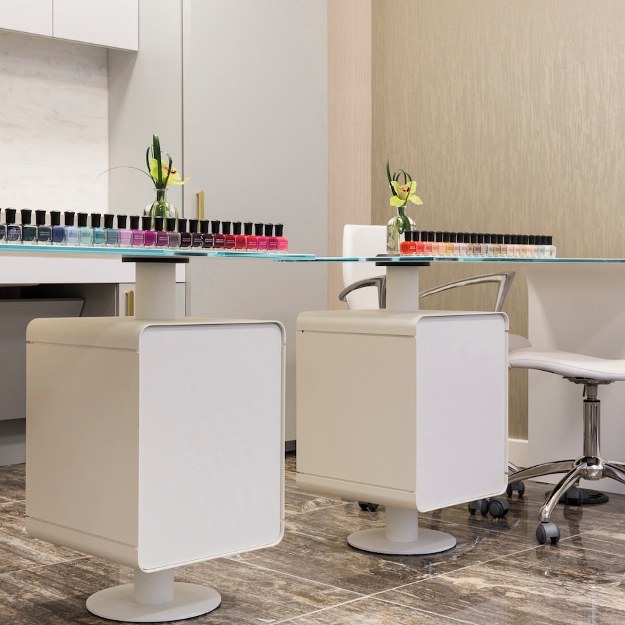 A modern salon with white chairs, a glass counter, and a selection of nail polish.