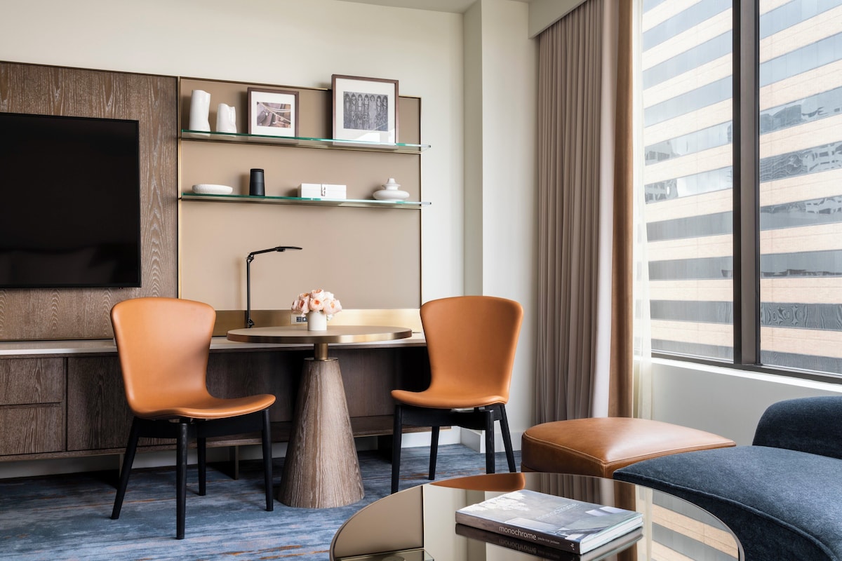 Une chambre d’hôtel équipée d’un bureau, de deux chaises, d’une télévision, d’une bibliothèque et d’une grande fenêtre.