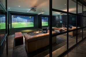 A modern room with a large TV displaying a sports game, leather seating, and a view through large windows.