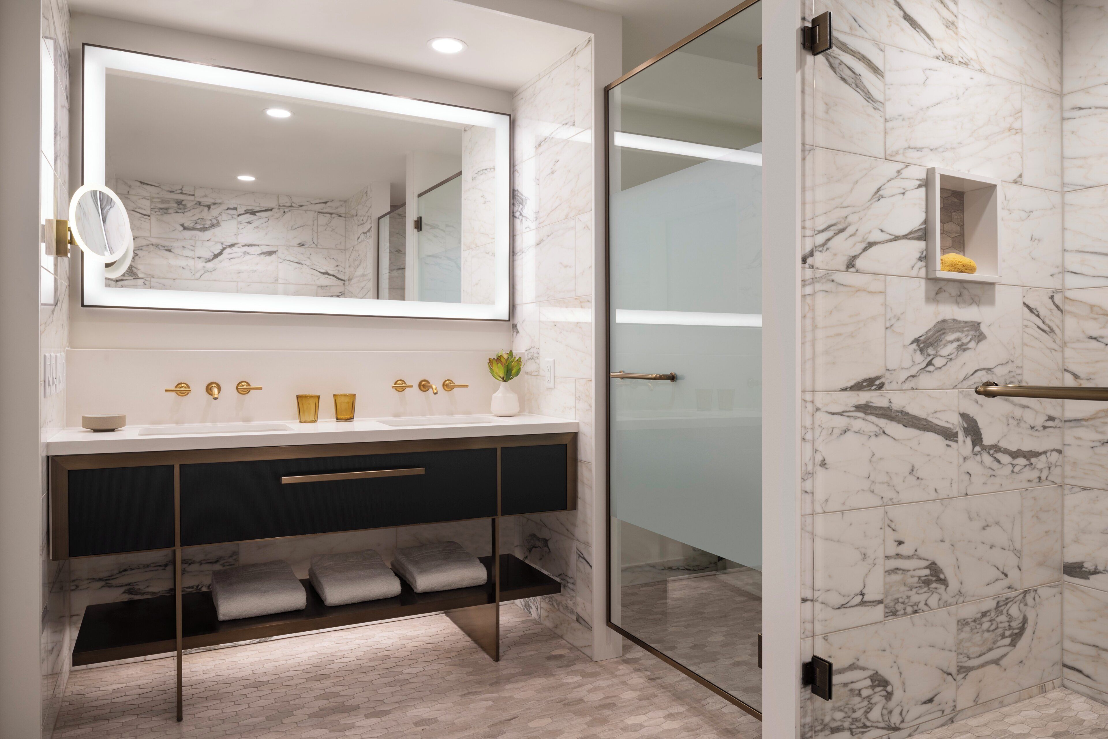A modern bathroom with a large mirror, marble tiles, a glass shower enclosure, and a vanity with a dark cabinet.