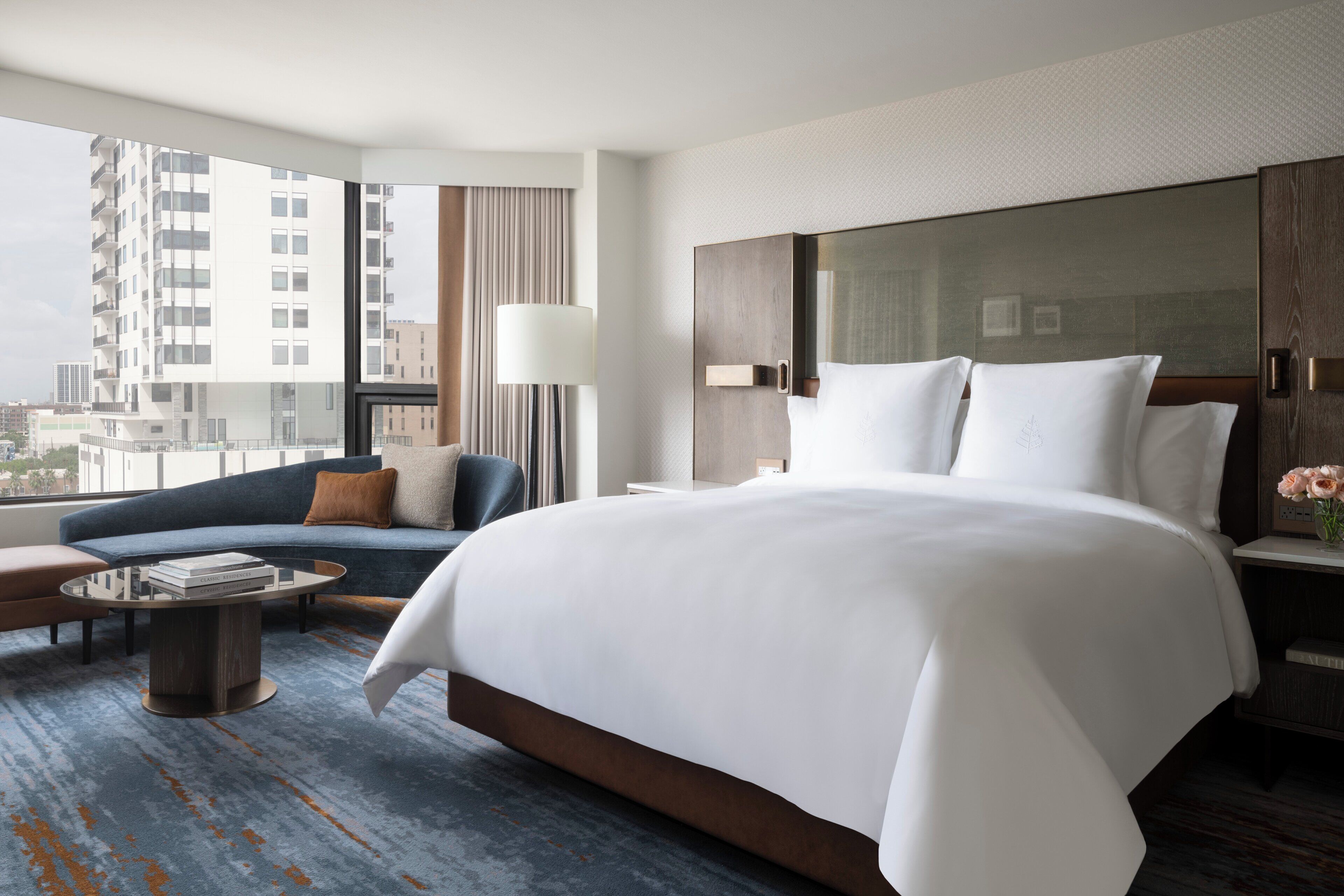 Habitación de hotel con una cama grande, un sofá, una mesita de café y vistas a la ciudad.