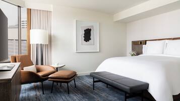 A modern hotel room with a large bed, a desk, a chair, and a bench.
