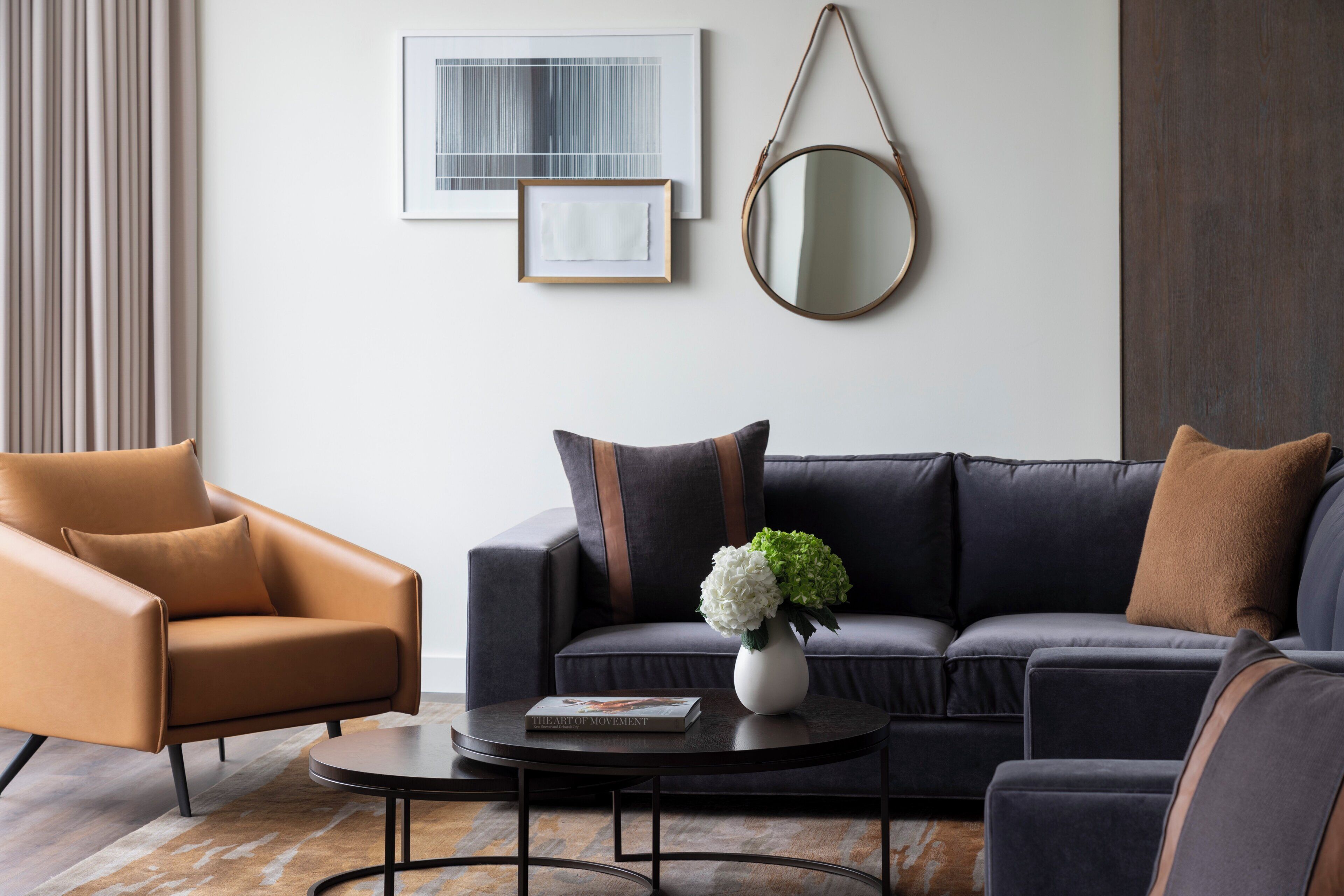 A modern living room with a leather armchair, a dark sofa, a round coffee table, and a vase with flowers.