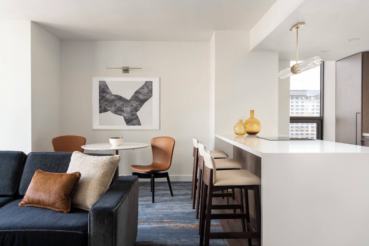 A modern kitchen with a white countertop, a hanging light fixture, and a city view through the window.