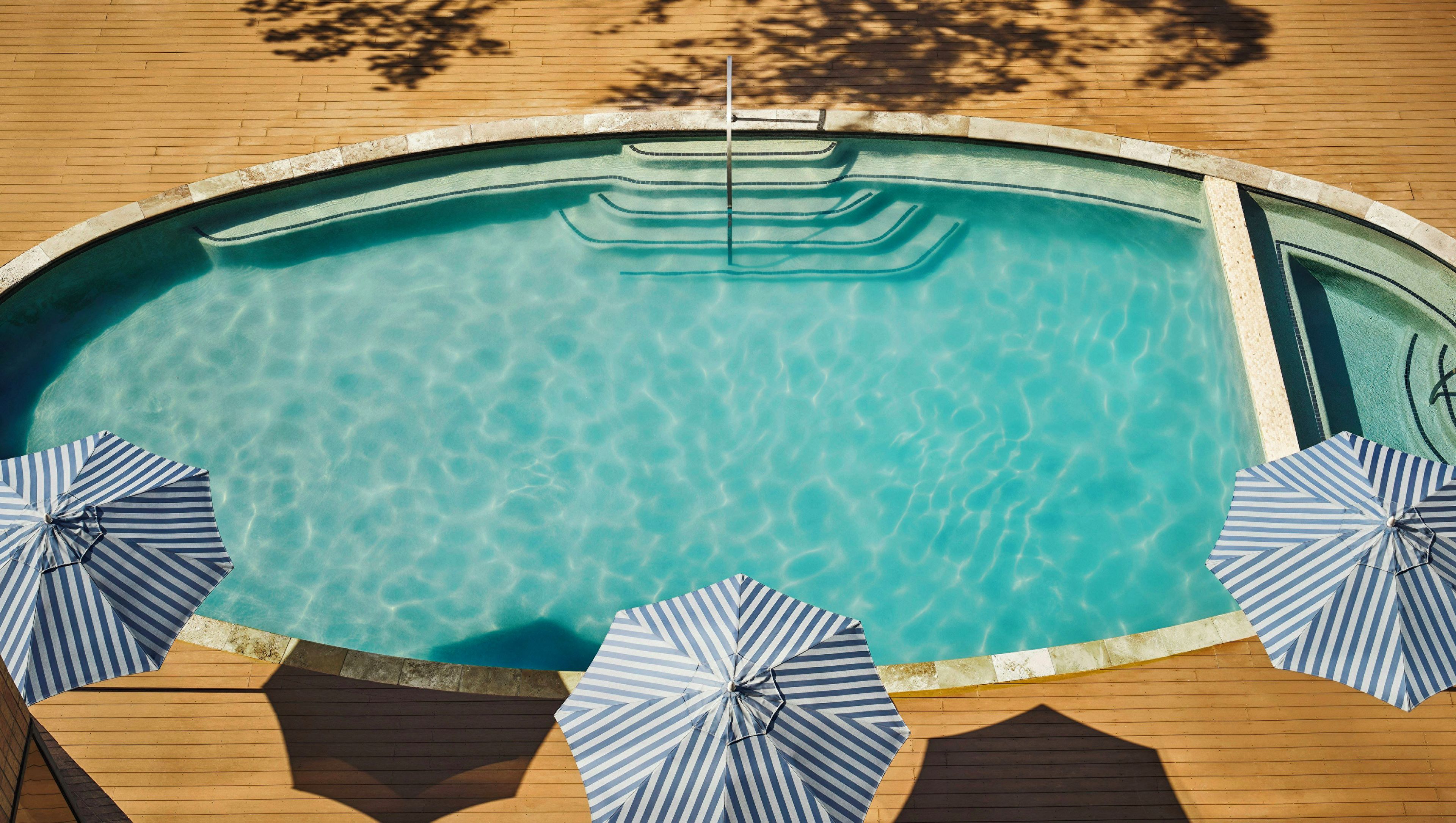 A clear swimming pool with a wooden deck and two striped umbrellas.