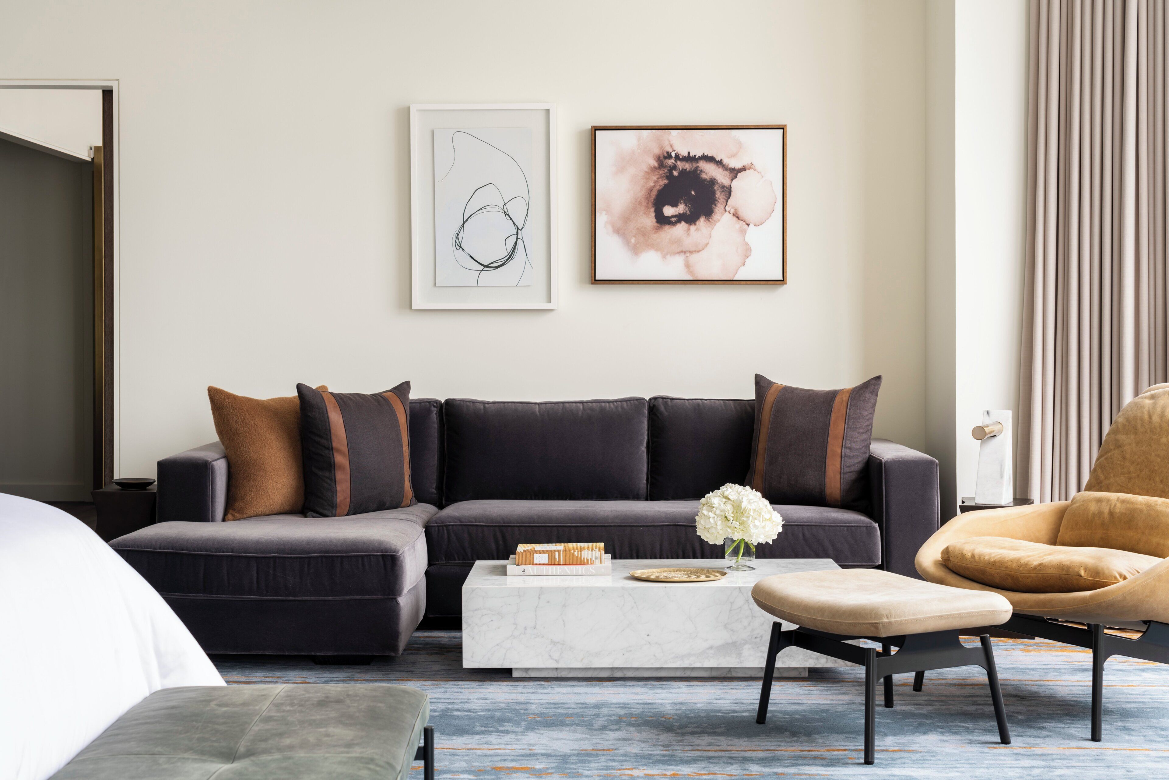 A modern living room with a dark grey sofa, a white coffee table, and a brown armchair. There are two framed artworks on the wall.