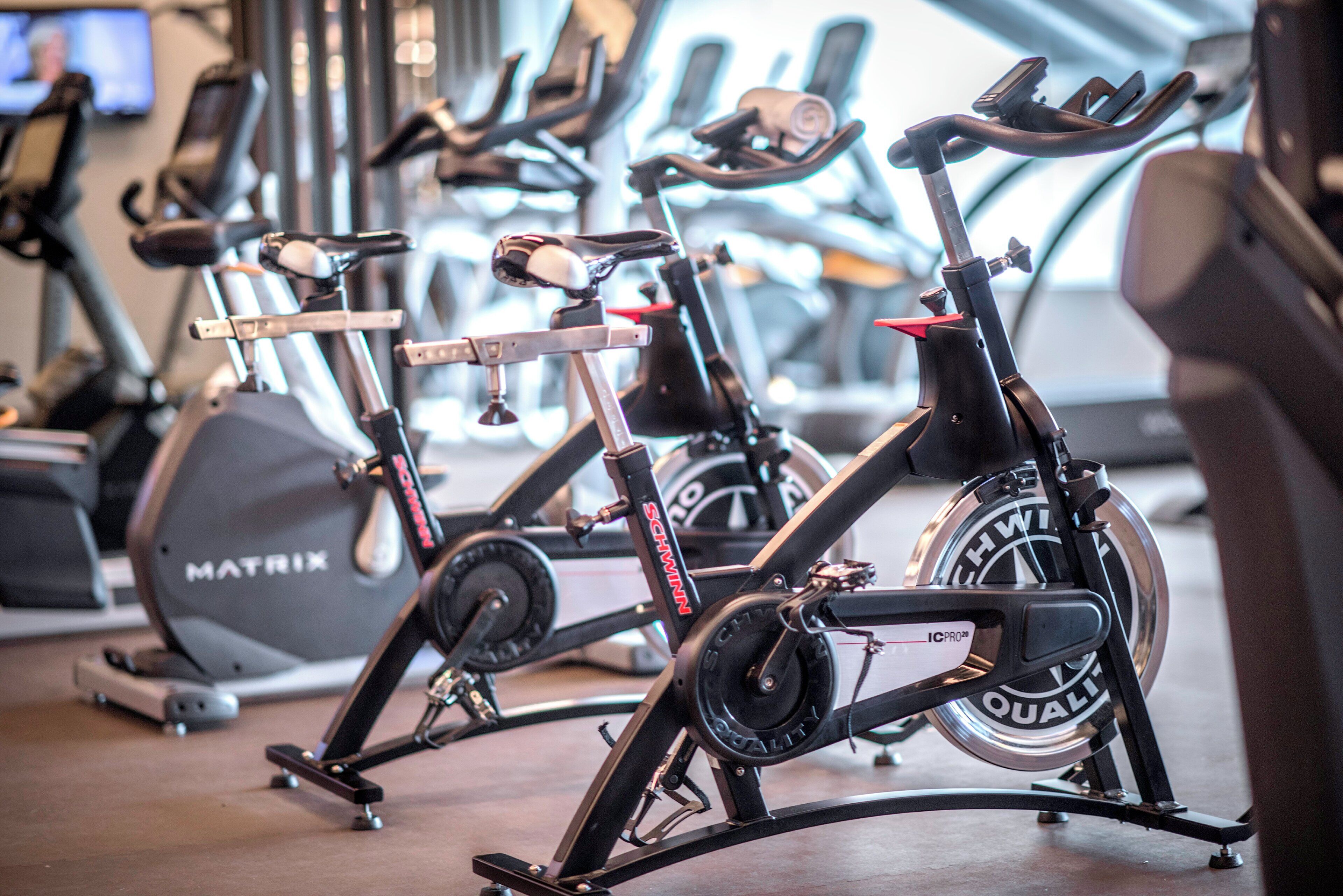 A stationary bike with a digital display and a red seat, positioned in a gym with other exercise equipment.